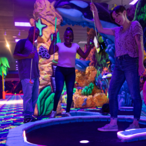 Three people cheering in celebration at an indoor mini golf hole with Putt Mania tech.