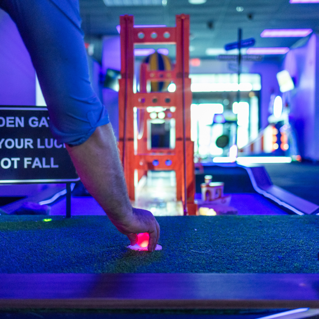 Hand setting a red illuminted Putt Mania golf ball on a tee on a Golden Gate Bridge themed golf hole.