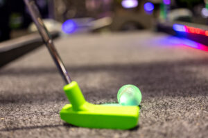 Green illuminated putt mania golf ball next to mini golf putter.