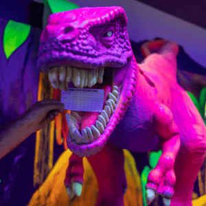 Paper mini golf scorecard being put in the mouth of a tee rex prop.