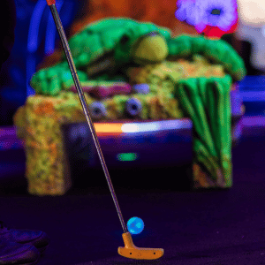 Orange mini golf putter with a blue light up golf ball on an indoor mini golf course.