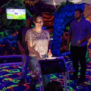 Woman tapping touchscreen on Putt Mania hole marker in an indoor glow mini golf course.