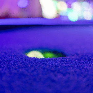 Illumnated green golf ball in cup on mini golf course.