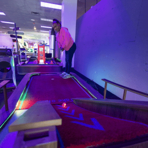 Woman putting a red illuminated golf ball up a ramp on an indoor mini golf course.