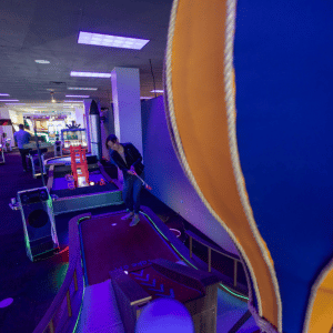 Woman putting a red illuminated golf ball up a ramp on an indoor mini golf course.