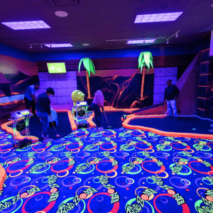 Four people putting on two different indoor mini golf holes.