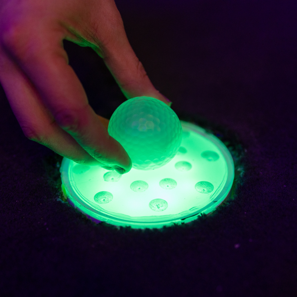 Glowing green Putt Mania golf ball being placed on glowing green golf tee.