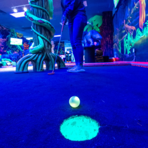 A glowing Putt Mania golf ball next to an illuminated golf hole with a person putting in the background.