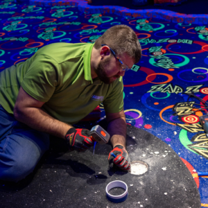 Man wearing a green shirt chiseling a hole in the floor for a Putt Mania tee.