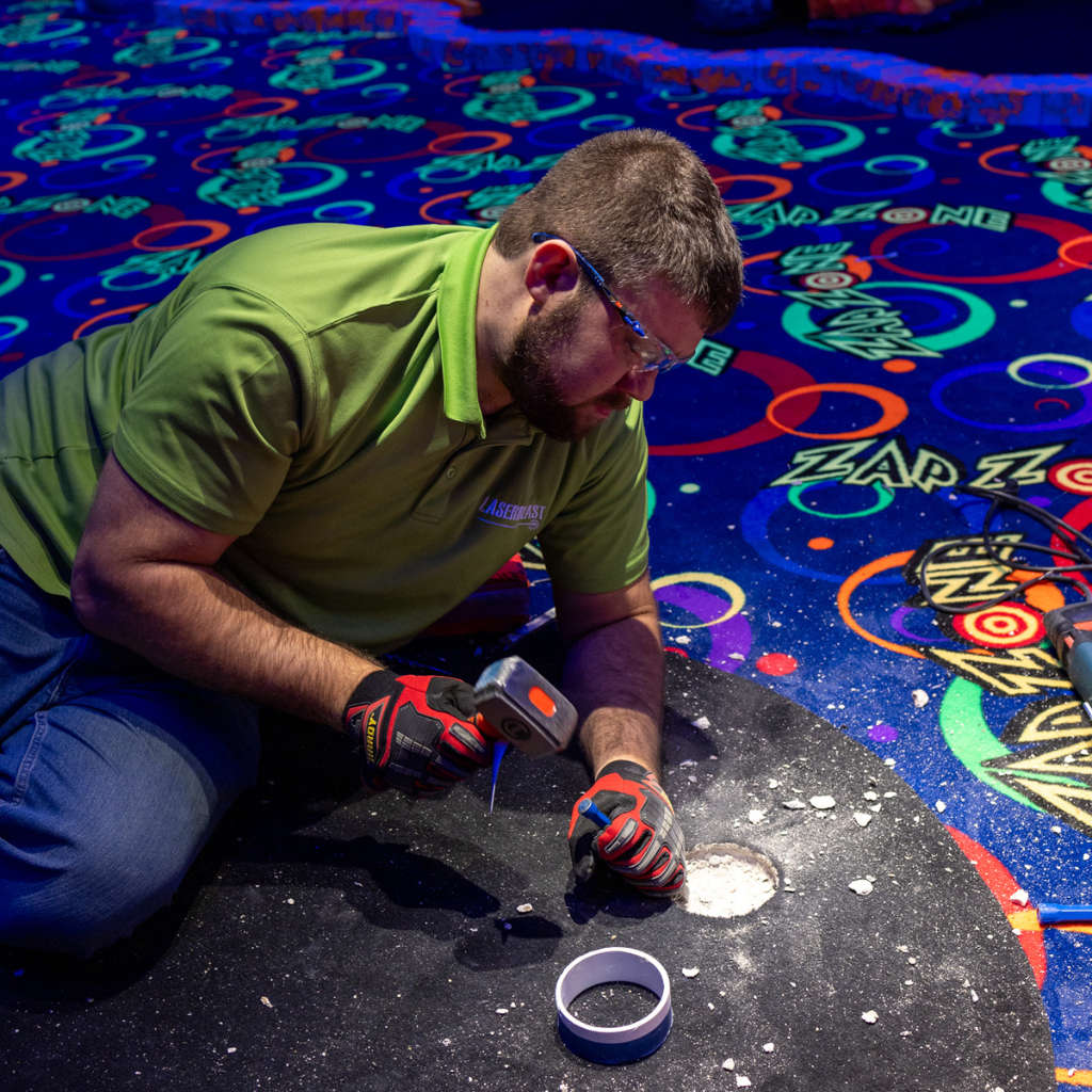 Man wearing a green shirt chiseling a hole in the floor for a Putt Mania tee.