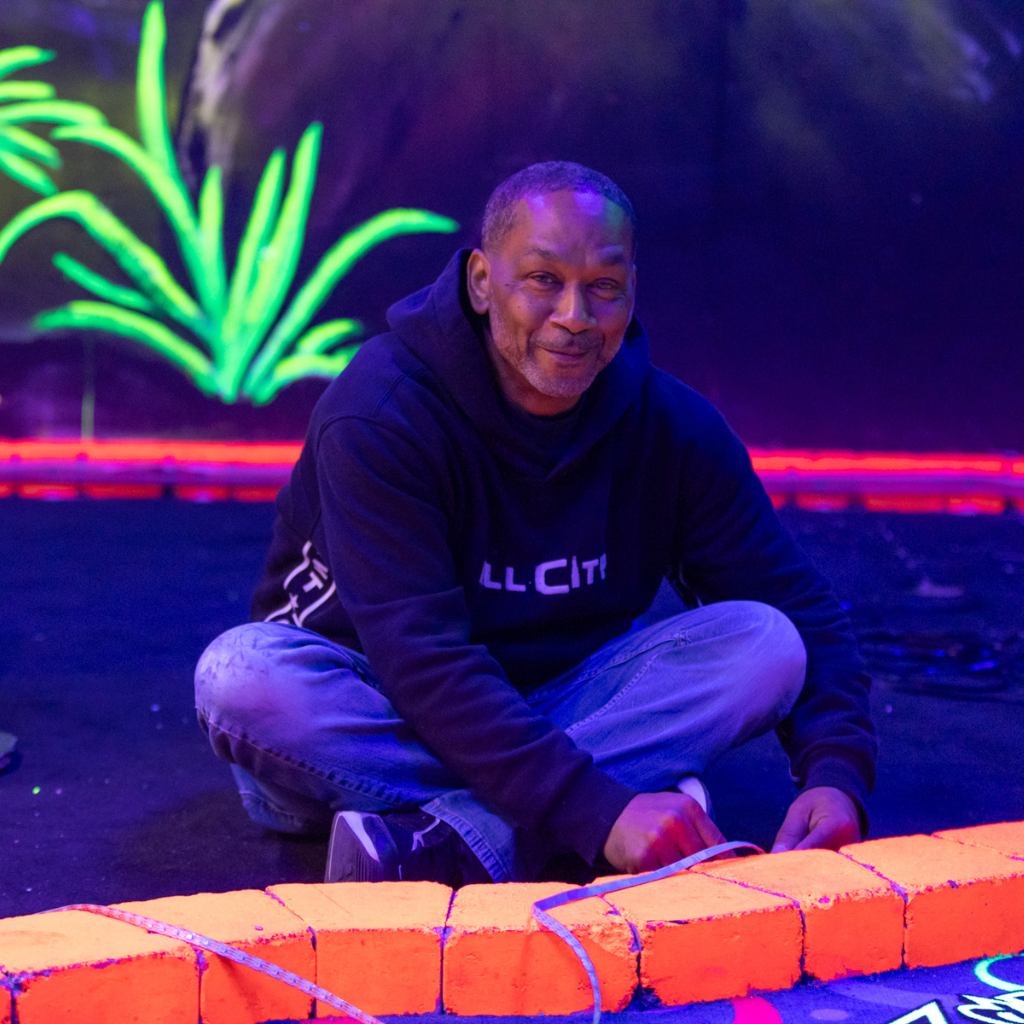 Man sitting on a glow mini golf course installing LED lights.