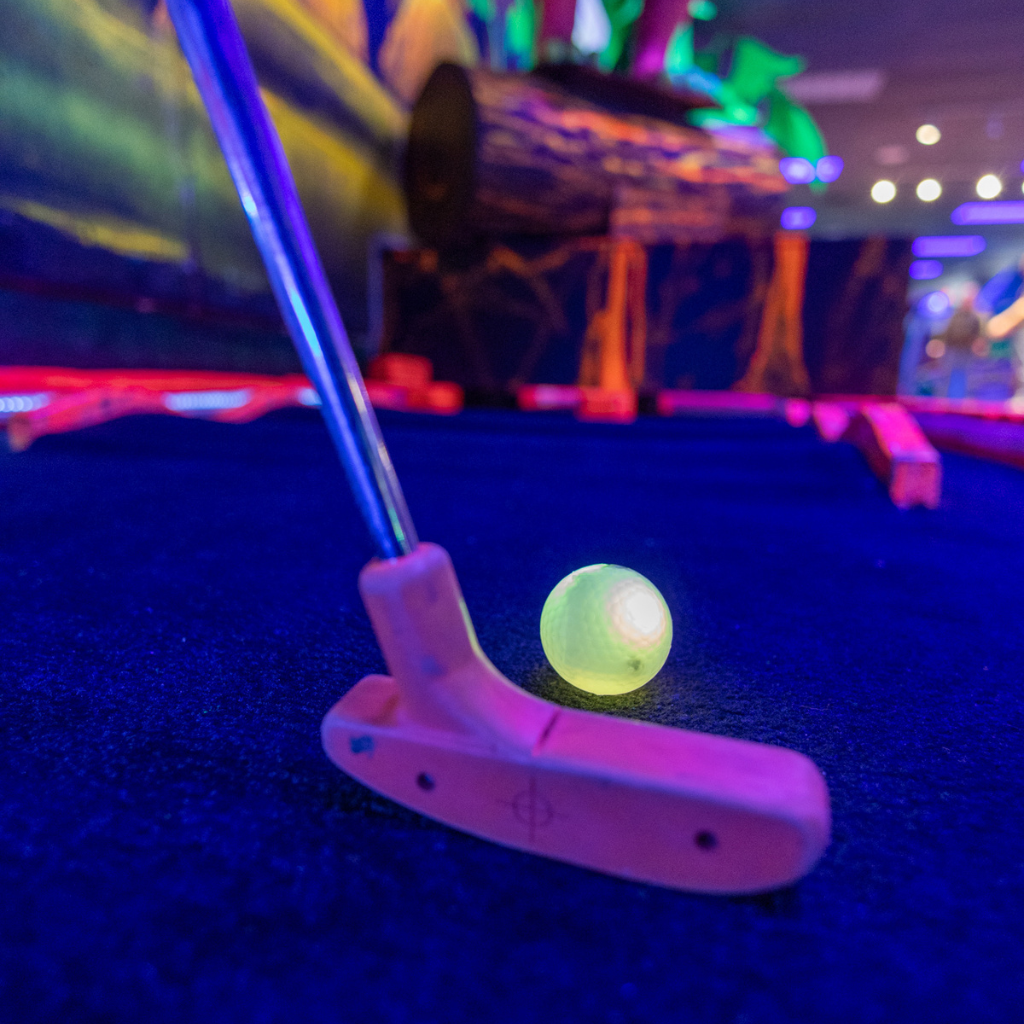 Yellow illuminated Putt Mania golf ball with a putter about to hit it on a glow golf course.