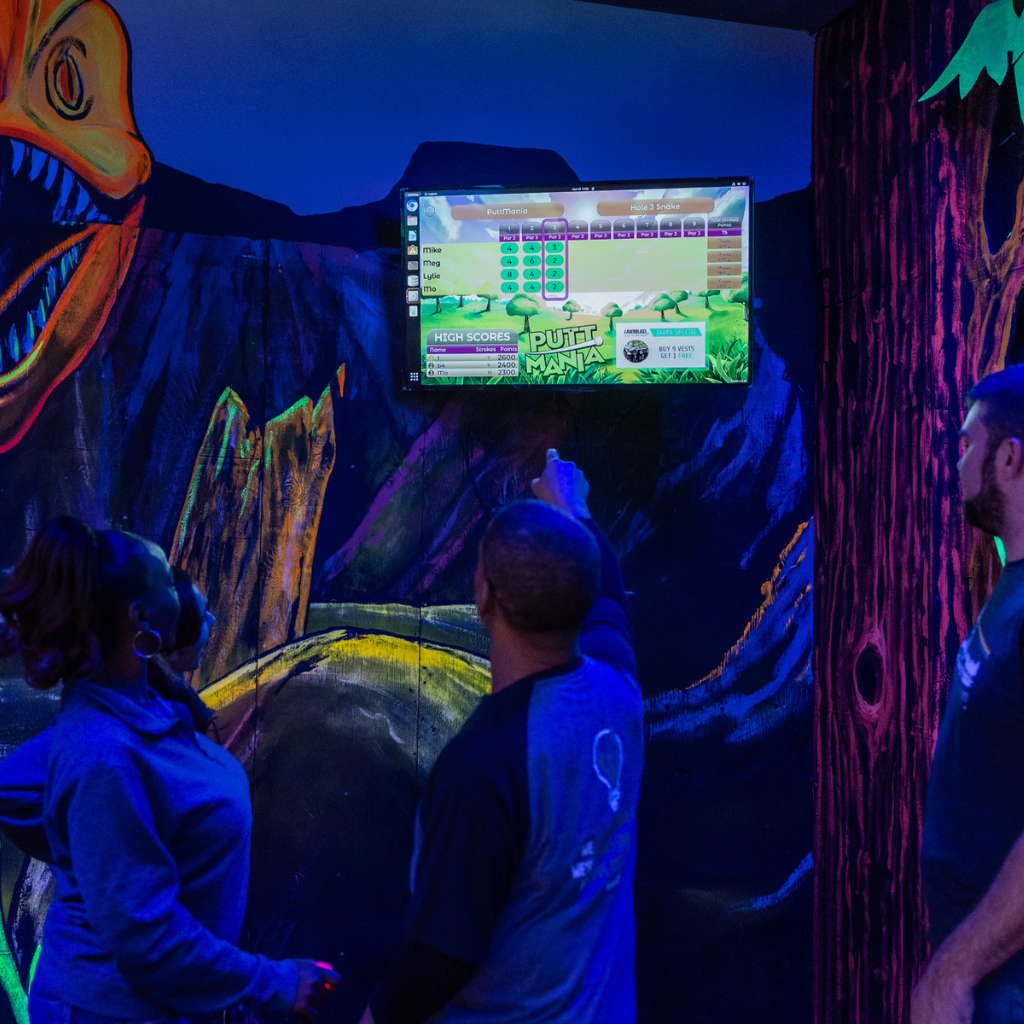 Three people on a mini golf course looking at the Putt Mania leaderboard.