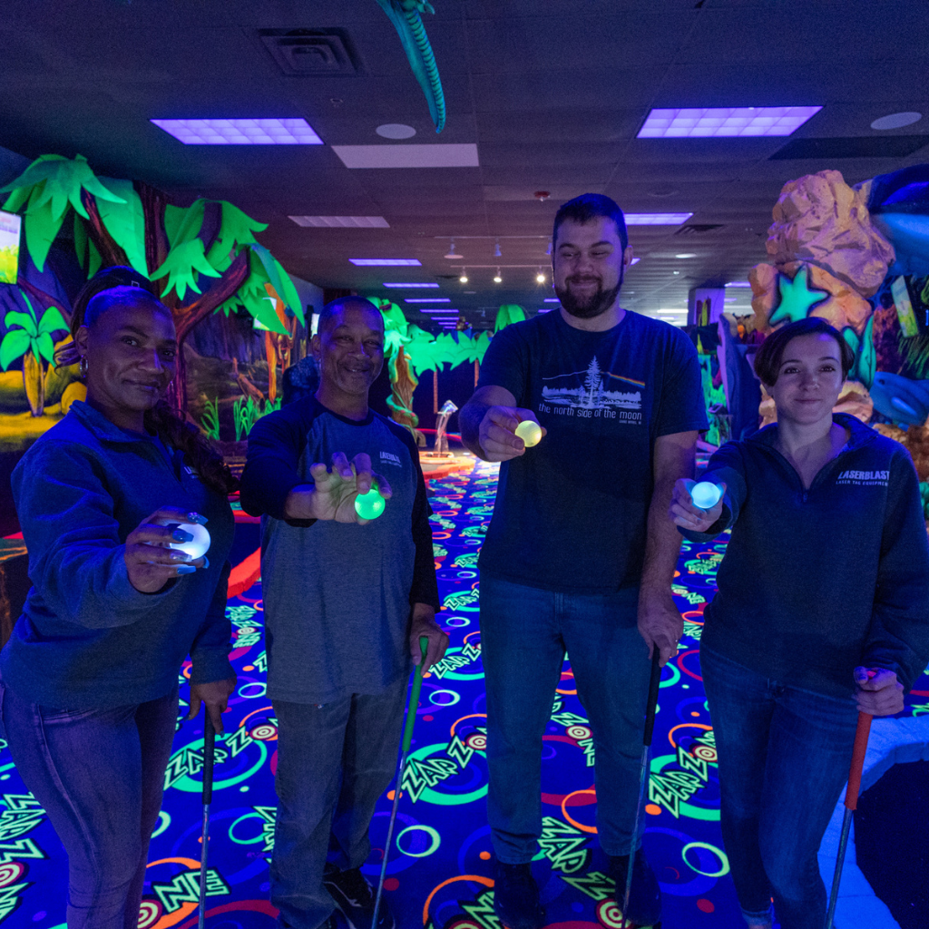 Four people standing in a row holding lit up Putt Mania golf balls out in front of them.