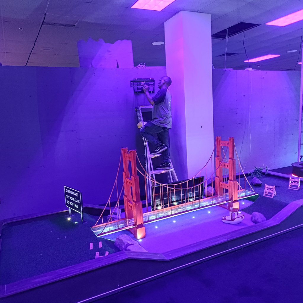 Man climbing up a ladder in a construction setting on an indoor mini golf course.