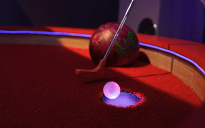 Illuminated Putt Mania ball being putted into the cup on a bowling themed mini golf hole with red carpet.