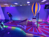 Woman putt off the tee on a hot air balloon theme indoor mini golf hole with Putt Mania tech.