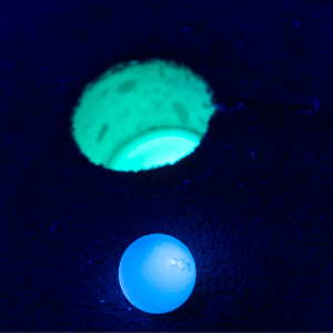 Illuminated blue Putt Mania golf ball next to a green illuminated Putt Mania cup with a dark background.