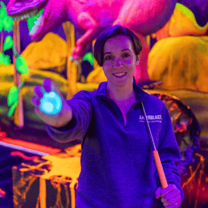 Woman holding out a blue illuminated Putt Mania golf ball with a putter over her other shoulder smiling at the camera.