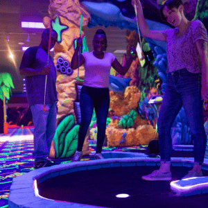 Three people cheering in celebration at an indoor mini golf hole with Putt Mania tech.