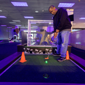 A man putting a golf ball into a cup on a soccer theme hole on an indoor mini golf course.