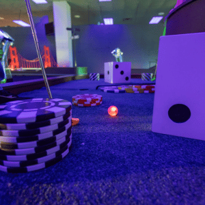 Illuminated Putt Mania golf ball on a casino themed indoor mini golf hole.