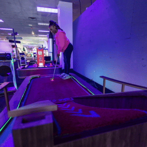 Woman putting a red illuminated golf ball up a ramp on an indoor mini golf course.