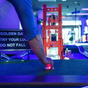 Hand setting a red illuminted Putt Mania golf ball on a tee on a Golden Gate Bridge themed golf hole.