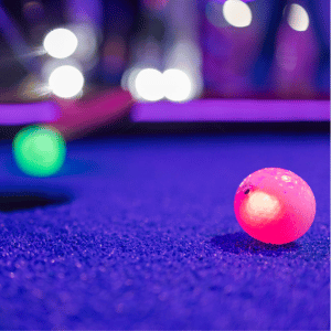 Red illuminated Putt Mania golf ball in foreground and green illuminated Putt Mania golf ball in background on an indoor mini golf course.