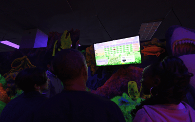 Three people looking up at a Putt Mania leaderboard at an indoor mini golf course.