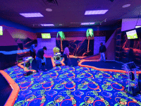 Four people putting on two different indoor mini golf holes.