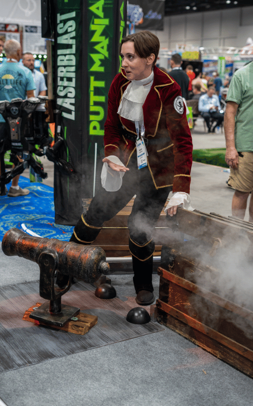 Woman in a pirate costume standing next to a cannon prop and a treasure chest prop with fog coming out of it.