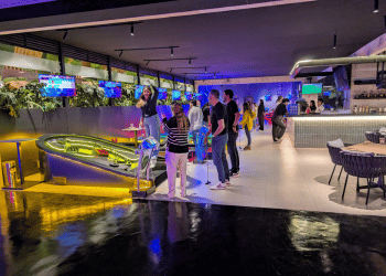 An indoor mini golf facility with groups of of people on the course playing mini golf.