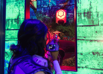 An individual wearing a laser tag vest facing away from the camera and aiming their phaser at a red laser tag base.
