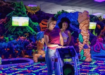 Two people in a dark light, neon mini golf environment, interacting with a Putt Mania digital hole marker.