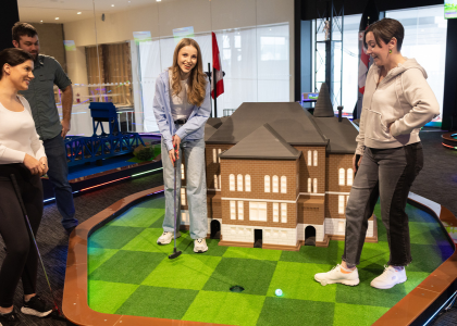 Three woman and one man on an indoor mini golf course with a large mansion prop.