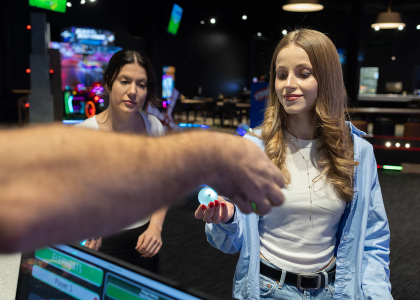 Two woman at the counter at a Family Entertainment Center with one of them being handed a golf ball.