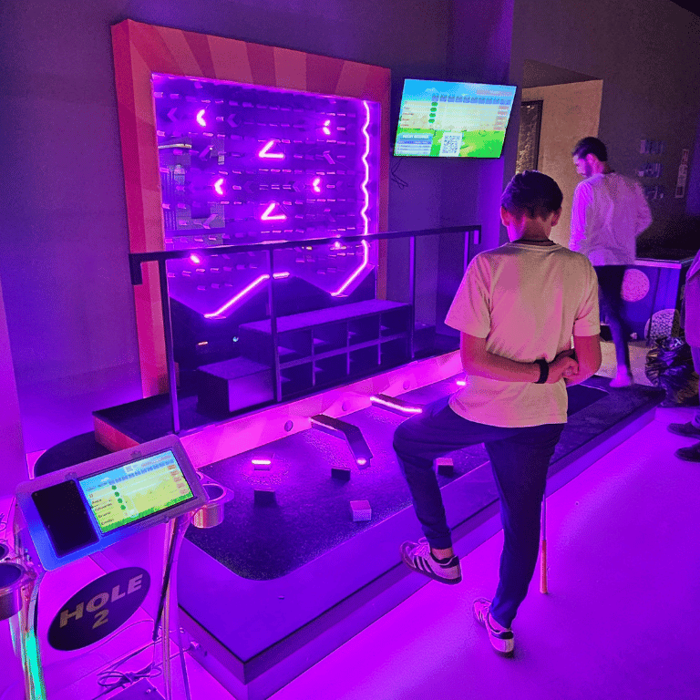 Plinko game style mini golf hole on indoor glow course with some people standing around course and Putt Mania technology.